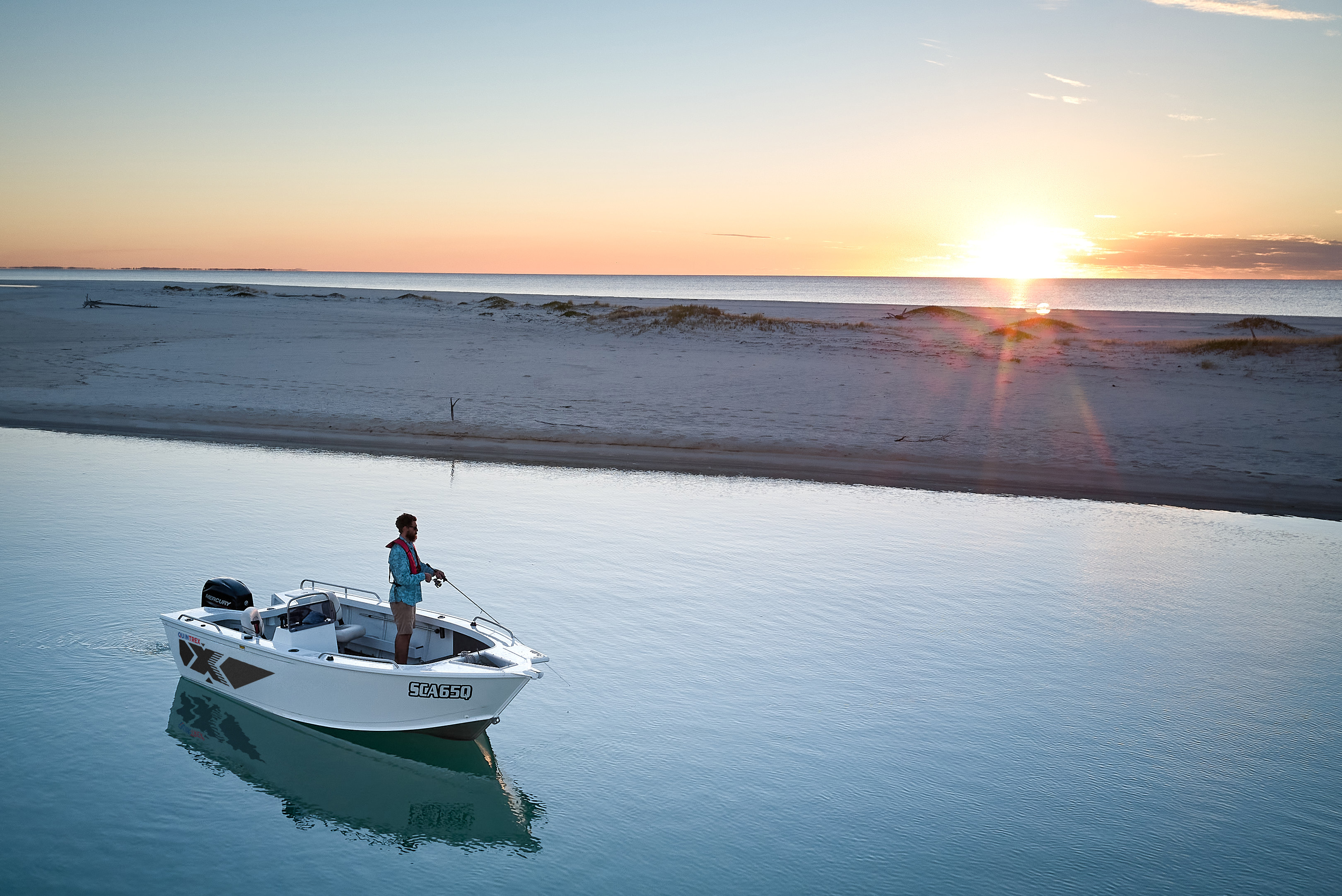 A Quintrex Renegade side console idling off a sandbar at sunrise with one angler standing on the casting deck